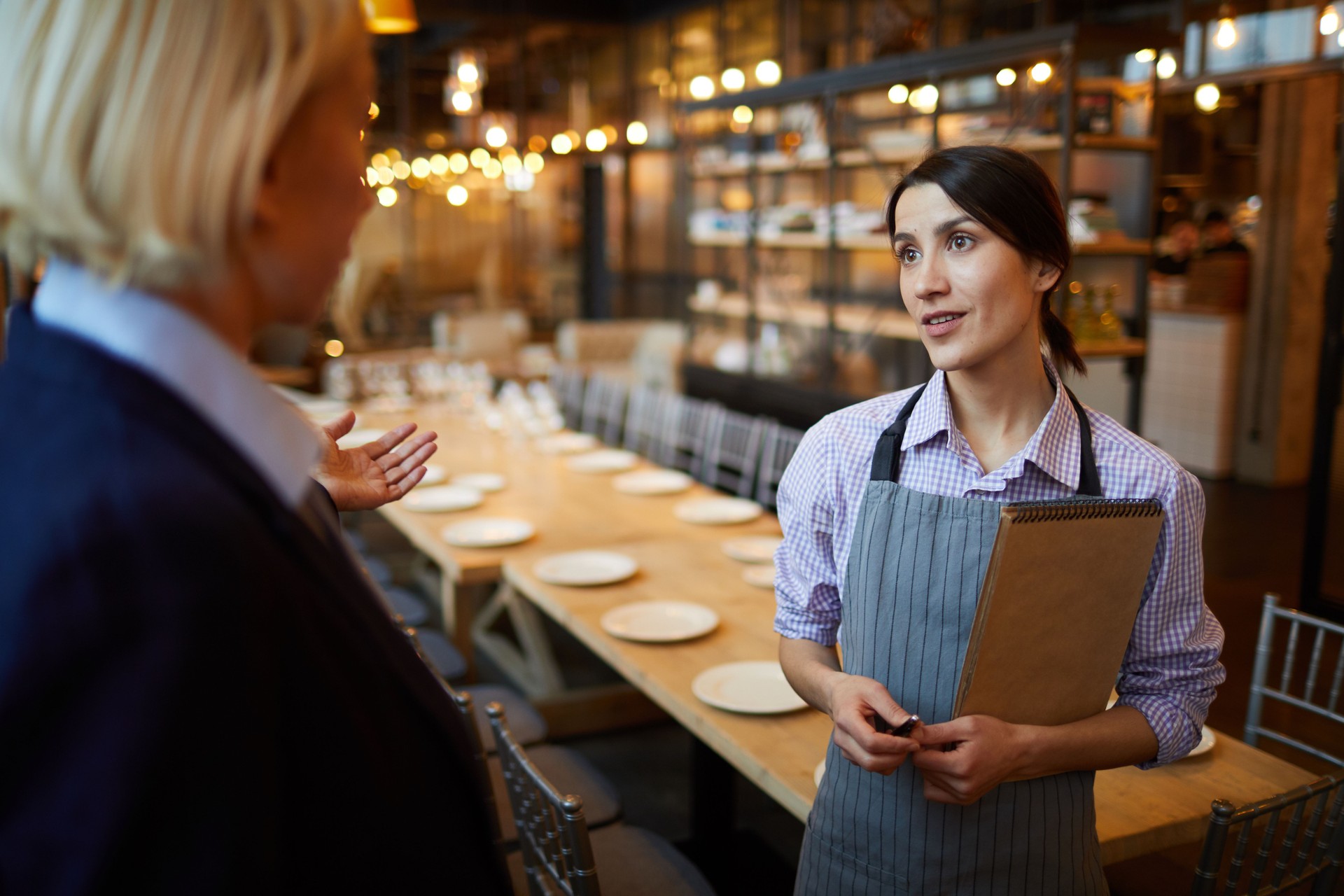 Restaurant manager talking to young waitress with notepad: strict manager asking report from waitress responsible for banquet