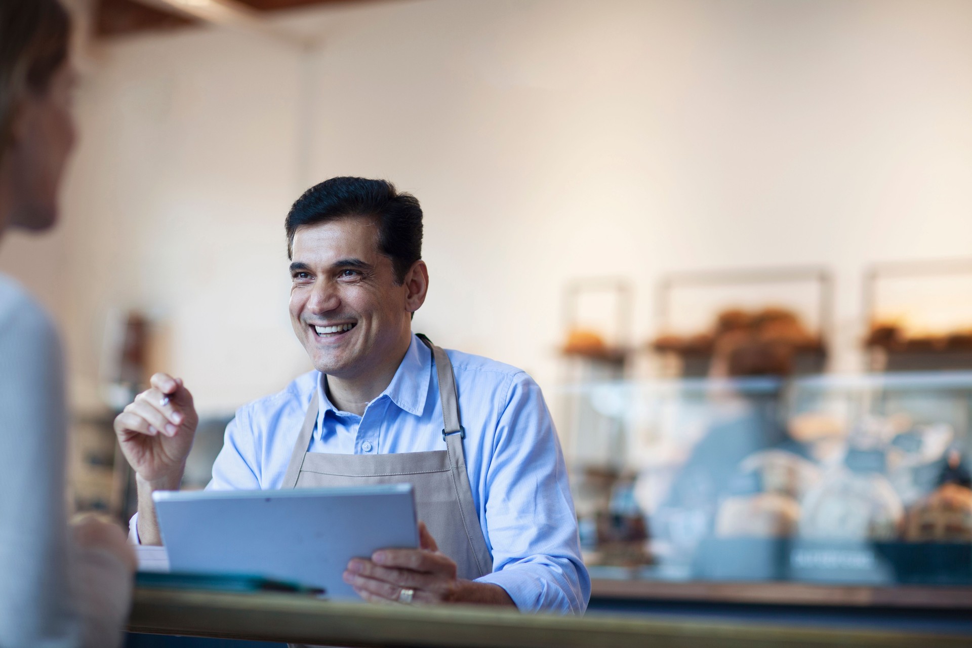 Middle Eastern mature man owner staff employee smiling using digital tablet planning small business in bakery cafe with woman financial advisor insurance agent colleague